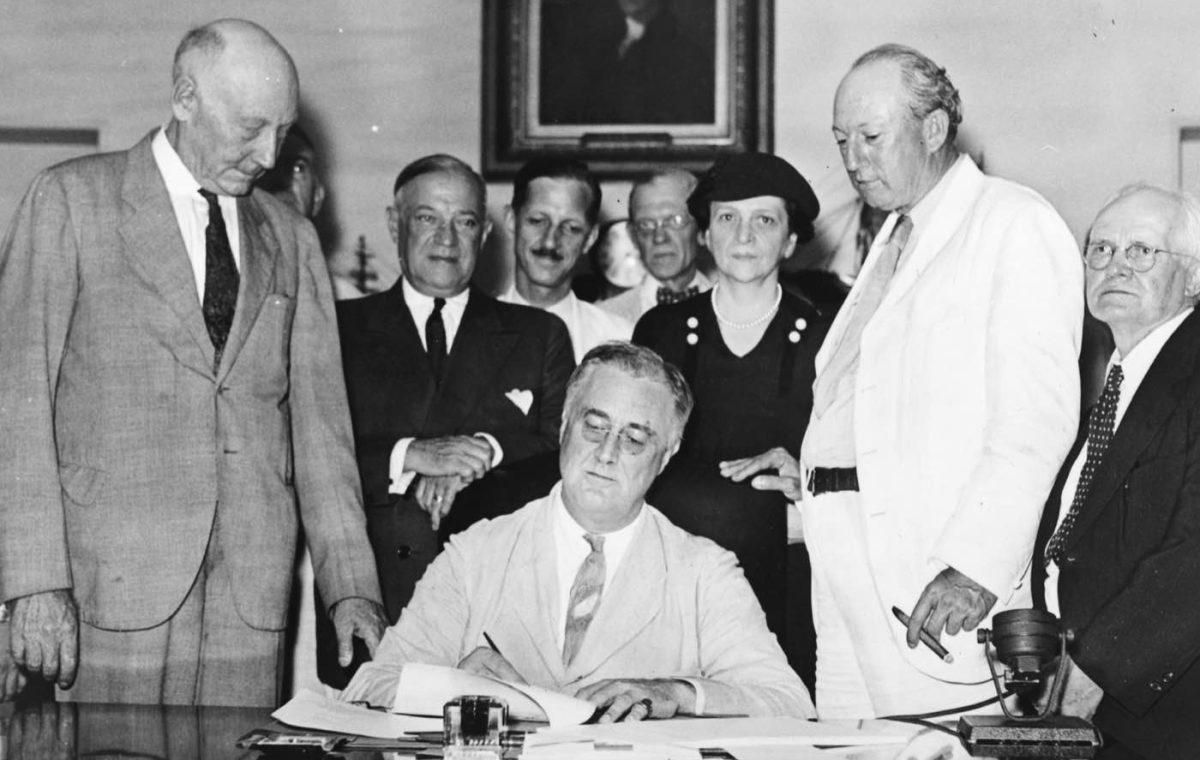 President Franklin Roosevelt signs the Social Security Act in 1935 as members of Congress and Labor Secretary Frances Perkins look on