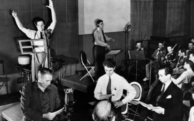 Orson Welles conducting with both arms raised at a CBS microphone during a Mercury Theatre radio rehearsal in 1938